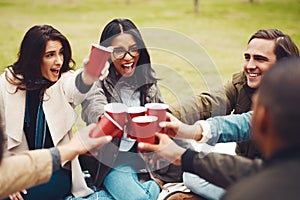 Celebrating life. a group of cheerful young friends having a picnic together while celebrating with a toast outside in a