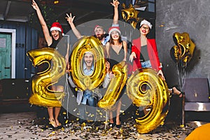 Celebrating New Year party. Group of cheerful young girls in beautiful wearing carrying gold colored numbers 2019 and