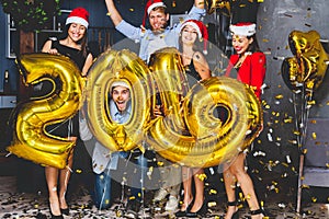 Celebrating New Year party. Group of cheerful young girls in beautiful wearing carrying gold colored numbers 2019 and