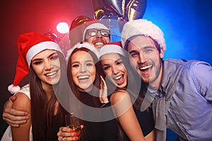 Celebrating New Year together. Group of beautiful young people in Santa hats throwing colorful confetti, looking happy