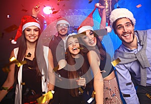 Celebrating New Year together. Group of beautiful young people in Santa hats throwing colorful confetti, looking happy