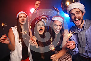 Celebrating New Year together. Group of beautiful young people in Santa hats throwing colorful confetti, looking happy