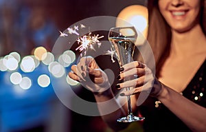 Celebrating New Years Eve, happy woman toasting with champagne, holding sparkler or bengal light