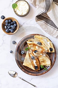 Celebrating Pancake day, healthy breakfast. Delicious homemade crepes with blueberries and ricota on a stone tabletop. Top view photo