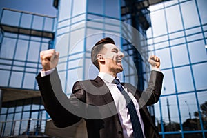 Celebrating success. Excited young businessman keeping arms raised and expressing positive while standing outdoors with office bui