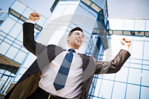 Celebrating success. Excited young businessman keeping arms raised and expressing positive while standing outdoors with office bui