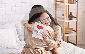 Celebrating together. Cute girl with mother`s day card hugging her mummy at home, panorama