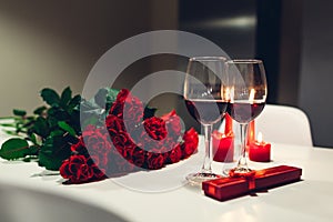 Celebrating Valentine`s Day with wine, candles, roses and gift box at home. Romantic atmosphere for lovers