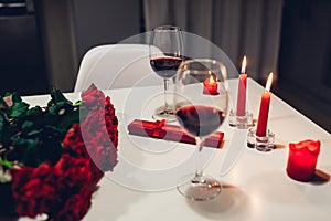 Celebrating Valentine`s Day with wine, candles, roses and gift box at home. Romantic atmosphere for lovers