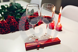Celebrating Valentine`s Day with wine, candles, roses and gift box at home. Romantic atmosphere for lovers