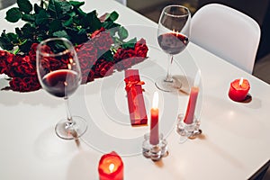 Celebrating Valentine`s Day with wine, candles, roses and gift box at home. Romantic atmosphere for lovers