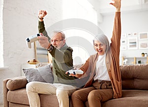 Overjoyed senior couple celebrating victory while playing video games at home