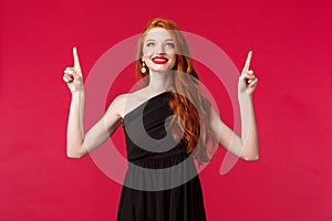 Celebration, events, fashion concept. Portrait of elegant and dreamy sensual redhead woman in black dress, pointing