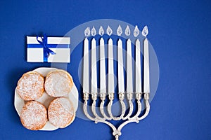 Celebration of Hanukkah. Candlestick with fried donuts, gift, on white and blue background