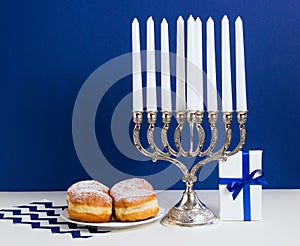 Celebration of Hanukkah. Candlestick with fried donuts, gift, on white and blue background