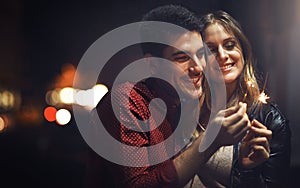 In celebration of our love...a happy young couple celebrating with sparklers outside at night.