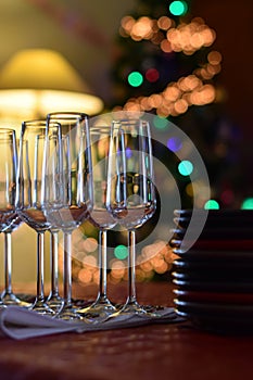 Celebration table with champagne glasses and stacked plates on christmas tree background