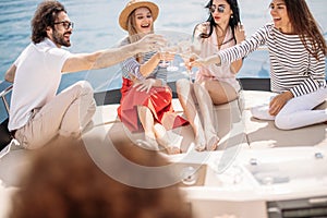 Happy friends clinking glasses of champagne and sailing on yacht