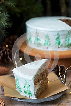 Celebratory cake decorated with painted Christmas trees on a dark background of branches and cones. Rustic style.