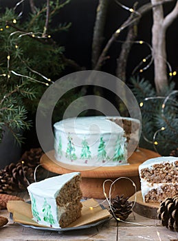 Celebratory cake decorated with painted Christmas trees on a dark background of branches and cones. Rustic style.