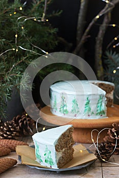 Celebratory cake decorated with painted Christmas trees on a dark background of branches and cones. Rustic style