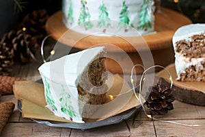 Celebratory cake decorated with painted Christmas trees on a dark background of branches and cones. Rustic style