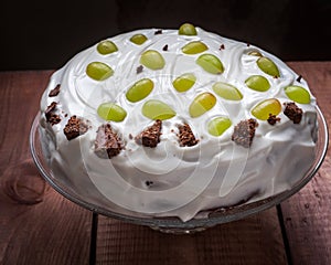 Celebratory homemade cake with cream and fruit on a glass cake, close-up, wooden plank table
