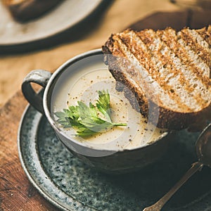 Celery cream soup and toast over linen tablecloth, square crop