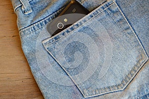 Cell phone in back pocket of short blue jean pant on wooden board