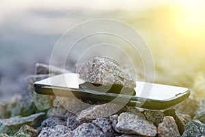 Cell phone with broken glass on gravel granite stones, unbreakable gadget, sun beam lights