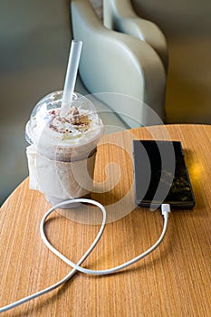 Cell phone charging in the cafe with a plastic cup of iced chocolate frappe photo