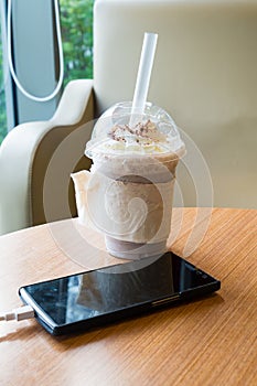 Cell phone charging in the cafe with a plastic cup of iced chocolate frappe photo