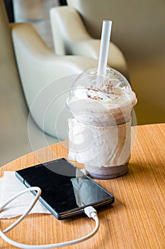 Cell phone charging in the cafe with a plastic cup of iced chocolate frappe photo