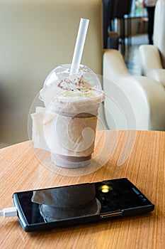 Cell phone charging in the cafe with a plastic cup of iced chocolate frappe photo