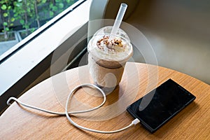 Cell phone charging in the cafe with a plastic cup of iced chocolate frappe photo