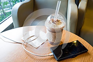 Cell phone charging in the cafe with a plastic cup of iced chocolate frappe photo