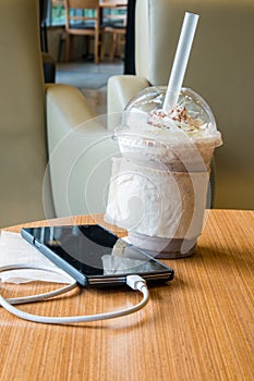 Cell phone charging in the cafe with a plastic cup of iced chocolate frappe photo