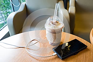 Cell phone charging in the cafe with a plastic cup of iced chocolate frappe photo