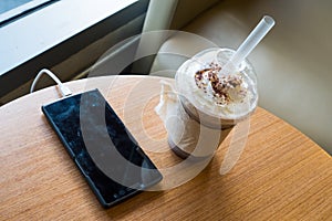 Cell phone charging in the cafe with a plastic cup of iced chocolate frappe photo