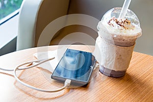 Cell phone charging in the cafe with a plastic cup of iced chocolate frappe photo