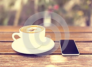 Cell phone and cup of coffee on a wooden table