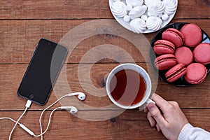 Cell phone with headphones, meringue, macaroons and a Cup of tea on wooden background