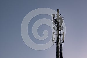 Cell phone tower / communications antenna or mast in silhouette at dusk against dark blue sky.