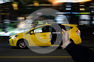 A cell phone with the the words rideshare on the screen on in front of a yellow taxi in the background. photo
