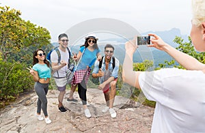 Cell Smart Phone Taking Photo Of Cheerful Tourist Group With Backpack Over Landscape From Mountain Top, People Posing