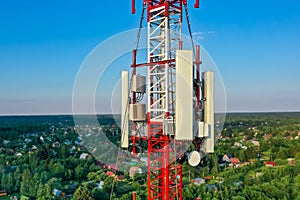 Cell tower against the background of a small village in the forest, Blue sky, shooting from a drone