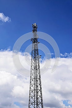 Cell tower against blue sky with clouds. A cell site or tower with antennae and telecommunications equipment is part of cellular