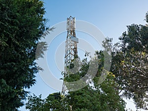 Cell tower / antenna mast in Porto, Portugal between trees with blue sky