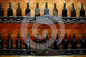 Cellar shelves with dark corked wine bottles against light brown wooden wall.