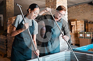 Cellar workers, making wine and mixing open tank with stirring, pressing and crushing tool for alcohol production. Happy